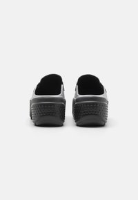 Des chaussures de style Crocs noires avec une semelle texturée, une tige lisse et un talon prononcé. L'arrière présente un logo en relief et une forme arrondie.