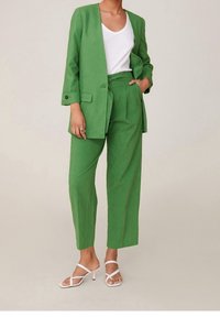 Zelený lněný blejzr s odpovídajícími kalhotami, s volným střihem a jedním knoflíkem. Doplněno bílým tílkem a sandály na podpatku.