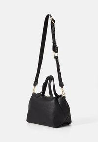 Svart strukturerad läderväska med dubbla handles upptill och ett avtagbart axelband med logotypdetaljer. Guldfärgade metalldetaljer.