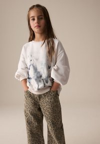 Sweat-shirt blanc avec un imprimé aquarelle de cheval, associé à un pantalon ample à motif léopard dans des tons terreux, présentant une texture douce.