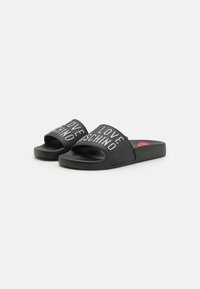 Black slide sandals with a textured sole, featuring "LOVE MOSCHINO" in rhinestones on the upper strap. Flat design, open toe.