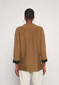 Pull en maille marron avec un col rond, des manches trois-quarts et des accents de poignets noirs. Texture douce avec une coupe décontractée.
