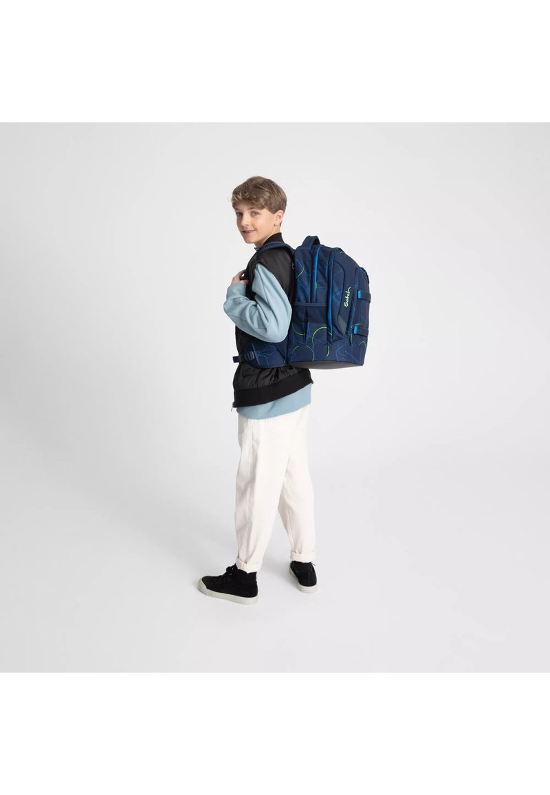 Sac à dos bleu marine avec des accents verts et des motifs géométriques, dotés de plusieurs compartiments et de bretelles ajustables. Le sac à dos est porté sur une épaule.