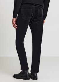 Schwarze Cordhosen mit schlanker Passform, ausgestattet mit zwei Gesäßtaschen, kombiniert mit schwarzen Stiefeletten. Glatte Textur und dezentes Rippenmuster.