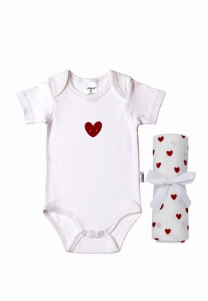 Weißer Baby-Body mit einem kleinen roten lächelnden Herz auf der Brust, neben einem aufgerollten weißen Tuch mit roten Herzmustern, das mit einem weißen Band gebunden ist.