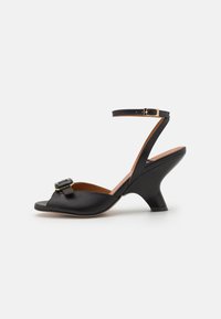 Black leather sandal with an open toe, featuring a decorative buckle and a mid-heel. Ankle strap secured with a gold-colored buckle.