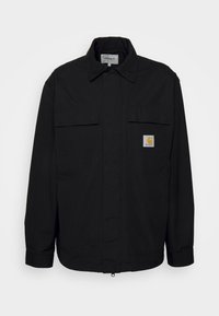 Black jacket made of durable fabric featuring a pointed collar, two chest pockets, and a small Carhartt logo patch on the left pocket.