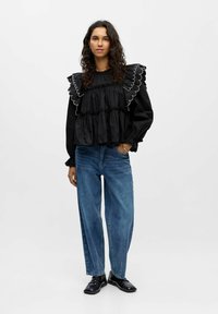 Blusa nera a balze con dettagli scallop, design a strati e maniche lunghe abbinata a jeans in denim blu chiaro a vestibilità larga e scarpe nere.