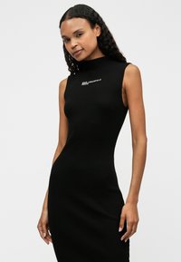 Μαύρο ριπ φόρεμα με ψηλό λαιμό και χωρίς μανίκια. Διαθέτει λευκό κεντημένο λογότυπο στο στήθος. Λείο υφή, εφαρμοστό σχέδιο.