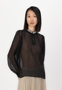 Blusa nera trasparente con scollatura arricciata, dettaglio a chiave e maniche lunghe a sbuffo, con un colletto decorativo di perline.