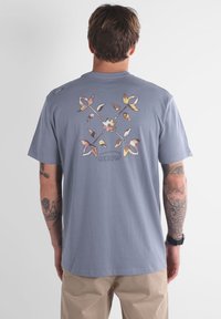T-shirt en coton gris avec un design floral coloré au dos. Manches courtes, encolure ronde, avec un logo Oxbow en dessous du graphisme.