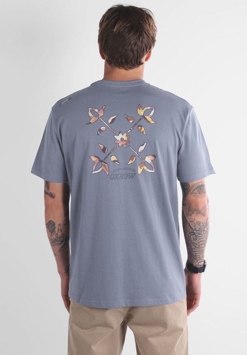 T-shirt en coton gris avec un design floral coloré au dos. Manches courtes, encolure ronde, avec un logo Oxbow en dessous du graphisme.