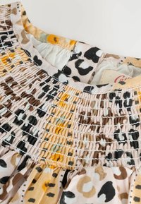 Könnyű anyagból készült, smockolt blúz, amely leopárdmintával rendelkezik bézs, barna és fekete árnyalatokban. Texturált gallér és gyűrt szegély.
