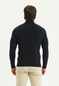 Pull à col roulé tricoté marine, design ajusté avec des manches longues et des poignets côtelés, texture lisse, associé à un pantalon beige clair.