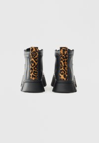 Crne kožne gležnjače s debelim crnim potplatom. Imaju panel od suknjice s leopard uzorkom straga, što dodaje teksturu i kontrast.