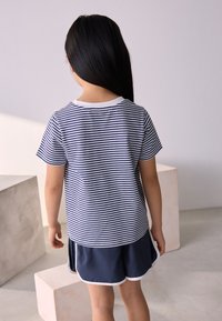 T-shirt en coton à rayures bleu marine et blanches avec un col rond blanc, associé à un short bleu marine avec un liseré blanc, vu de dos.