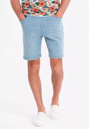 Shorts en denim bleu clair avec deux poches latérales, coupe droite et ourlet propre. Portés avec une chemise à motifs floraux et des chaussures à enfiler blanches.