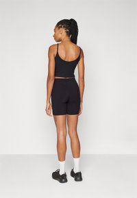 Svart ribbet crop top og matchende shorts, med en tett passform. Modellen har på seg svarte tøfler og hvite sokker, med håret i hestehale.