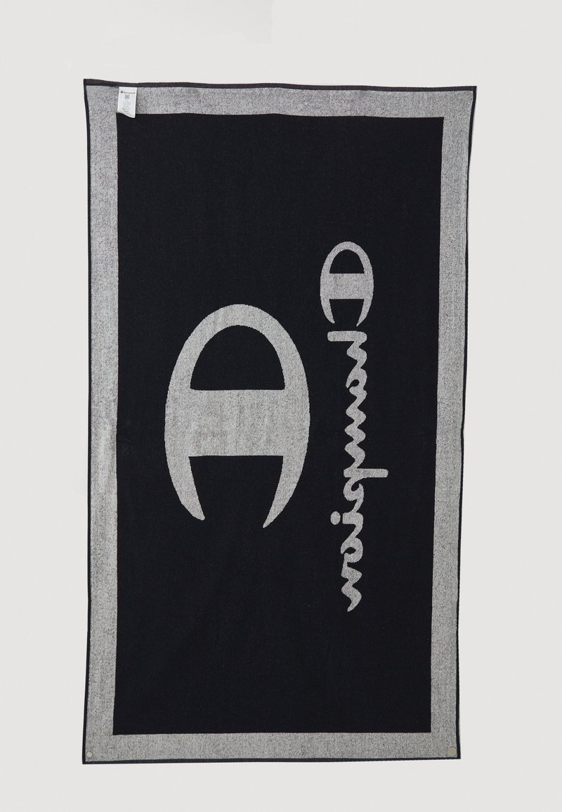 Pătură tricotată în nuanțe de negru și gri, cu un design stilizat al unui logo mare și text. Marginile sunt evidențiate cu o bordură contrastantă pentru a crea distincție vizuală.