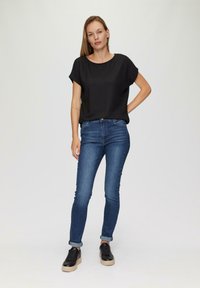 Zwarte cropped top met een gestructureerd ontwerp, gecombineerd met strakke donkerblauwe spijkerbroek en zwarte sneakers met een dikke beige zool.
