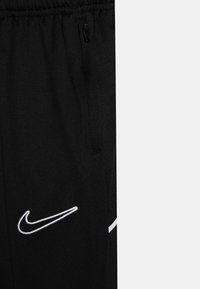 Zwarte stof met een wit Nike-swooshlogo dat is geborduurd vlak bij een ritssluitingzakje op sportieve broek of korte broek.