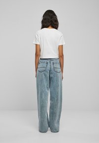 Kuttet hvit t-skjorte og vide lyseblå jeans med en falmet tekstur. Jeansene har to baklommer og en løs passform.
