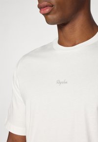 Hvid bomulds t-shirt med rund hals og korte ærmer, prydet med en diskret grå broderet "Rapha" logo på brystet. Glat tekstur.
