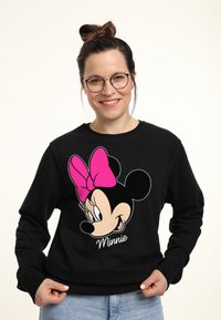 Felpa nera con una grafica colorata di Minnie Mouse, con un fiocco rosa e il nome "Minnie" stampato sotto. Tessuto morbido, vestibilità casual.