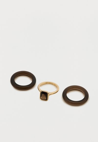 Deux bagues en résine marron et une bague en or avec une pierre noire rectangulaire, présentant une texture lisse et un design minimaliste.