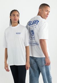 Hvide bomulds-T-shirts med blå grafiske tryk. Forsiden har teksten "DELIGHT," mens bagsiden viser et design af en drikkevare dåse samt yderligere tekstdetaljer.