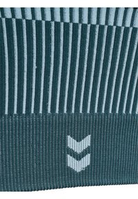 Tejido de punto en verde azulado oscuro con franjas alternas en azul claro. Presenta un pequeño logo blanco con un patrón de Chevron en la parte inferior.