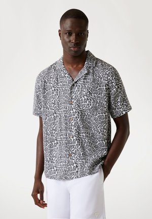 Short-sleeve button-up shirt in black and white featuring a swirling text pattern, with a relaxed fit and wooden buttons.