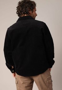 Zwarte corduroy shirt met een textuurstof, met een kraag en knoopmanchetten, gedragen over beige cargobroek.
