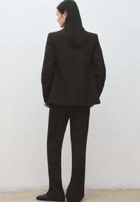 Brązowy dopasowany garnitur z lejącą się marynarką i szerokimi spodniami. Gładka faktura, strukturalny krój i otwarty tył.