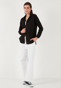 Black button-up shirt with a pocket, long sleeves rolled up, paired with white wide-leg pants and high-top black sneakers.