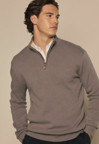 Grijze pullover trui met een halve ritssluiting en een kraag, gemaakt van gestructureerde stof, met ribgebreide cuffs en zoom, gecombineerd met een witte blouse met kraag.