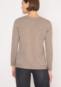Top beige a maniche lunghe realizzato in tessuto a maglia testurizzato, con scollatura rotonda e vestibilità rilassata, abbinato a jeans scuri.