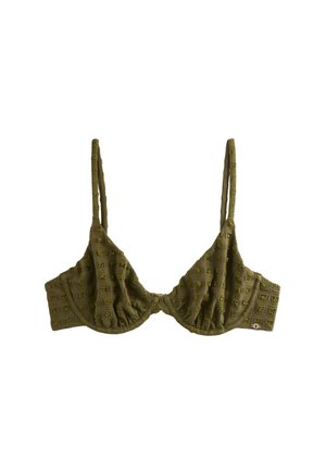 Kobieta w teksturowanym oliwkowozielonym bikini i bransoletkach stoi nad oceanem pod czystym niebem, patrząc w dal.