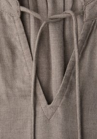 Gros plan d'un sweat à capuche en tissu taupe avec un col en V et un cordon de serrage noué en boucle au centre.