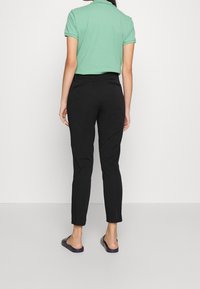 Svarta slim-fit byxor med en slät yta och två bakfickor, ihop med en mintgrön pikétröja. Utstrålar en avslappnad, modern stil.