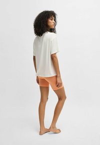 Lightweight, cream short-sleeve top paired with orange form-fitting shorts, smooth fabric, and a relaxed fit, viewed from the back.