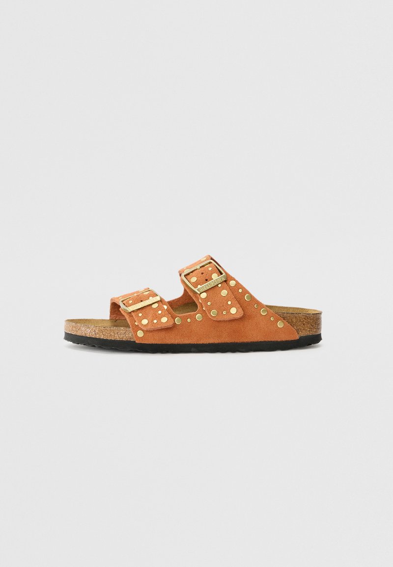 Sandali in suede marrone con due cinturini regolabili, accessori in oro e dettagli a borchie circolari. Sottopiede in sughero e suola in gomma nera.