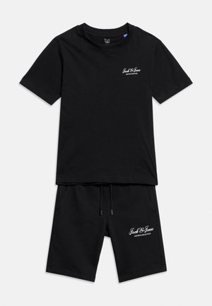 Set composto da t-shirt nera a maniche corte e pantaloncini con la scritta bianca "Jack & Jones Archive Selection" sul petto e sulla gamba sinistra, poggiato su uno sfondo bianco.