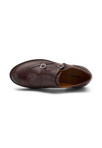 Scarpa in pelle marrone con dettagli brogue, due cinturini con fibbia e punta arrotondata. Presenta accenti perforati e una suola testurizzata.