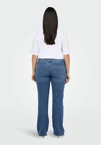 Jean bleu évasé avec une taille mi-haute, comportant deux poches arrière et des détails de couture subtils, associé à un t-shirt blanc uni.