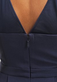 Gros plan du dos d'une robe bleu marine avec une fermeture éclair visible partiellement fermée sur la peau exposée en haut du dos.