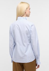 Camicia a righe blu con colletto e polsini arricciati. Presenta maniche lunghe, polsini con bottoni e sottili dettagli marroni sulle righe verticali.