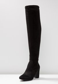 Botas negras hasta la rodilla hechas de suave ante, con un diseño ajustado, puntera redonda y un tacón grueso. Textura suave sin patrones visibles.