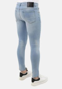 Lichtblauwe denim skinny jeans met een vervaagde afwerking, vijf zakken en een zwart leren label op de tailleband. Draagt met witte sneakers.