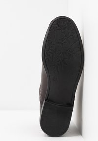 Semelle d'une chaussure brun foncé montrant une semelle extérieure en caoutchouc noir avec un motif floral et un talon texturé.